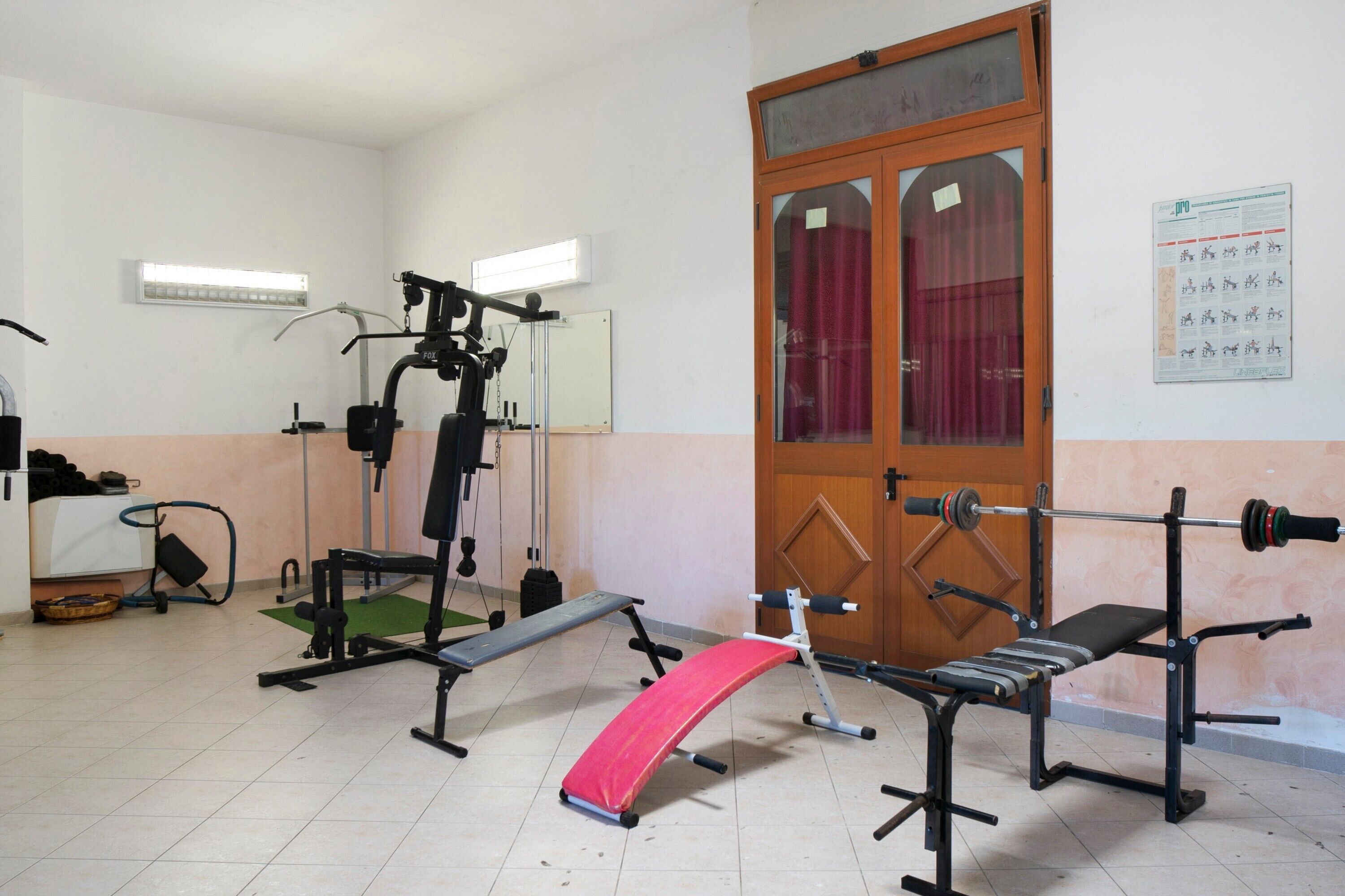 Een sportschool met trainingsapparatuur, een bank en een deur met een prikbord.