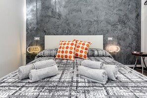 A modern bedroom with a patterned bedspread, two pillows with orange polka dots, and two bedside lamps.