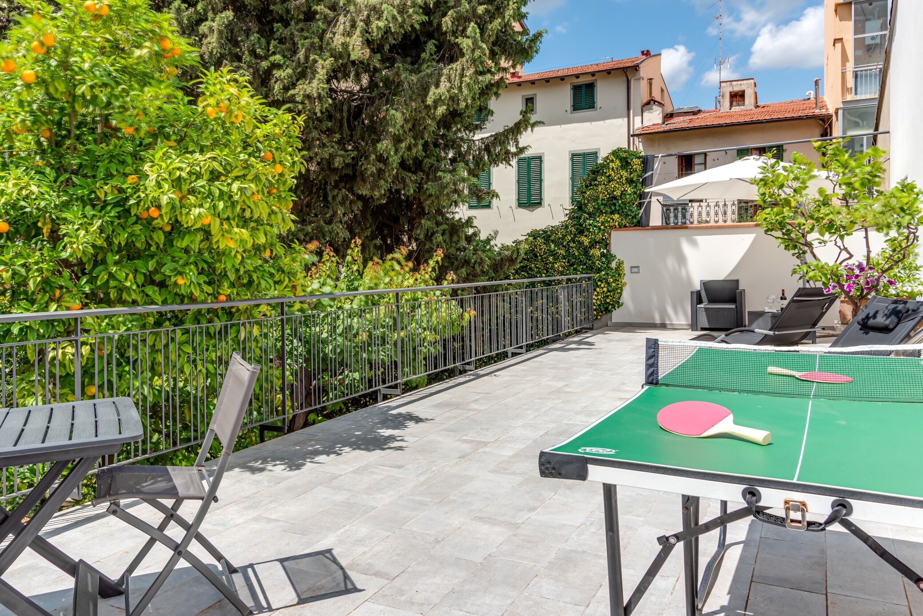 An outdoor table tennis setup with a net, two paddles, and a chair.