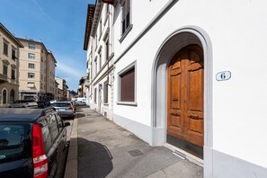 A street view with parked cars, a white building with a large wooden door, and a number '6' sign.