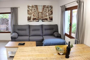 A modern living room with a grey sofa, a wooden coffee table, a wine bottle, and a bowl of fruit.