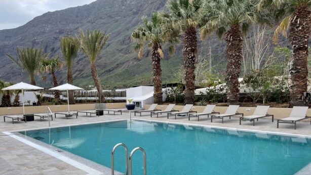 A swimming pool with lounge chairs and umbrellas, surrounded by palm trees and mountains. - Apartment 'Finca Wapa - Finca' with Sea View, Wi-Fi and Air Conditioning (Frontera)