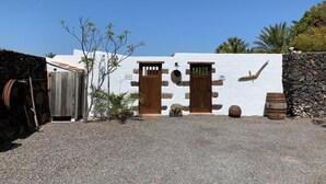 Un edificio con dos puertas de madera, un muro de piedra y suelo de grava.