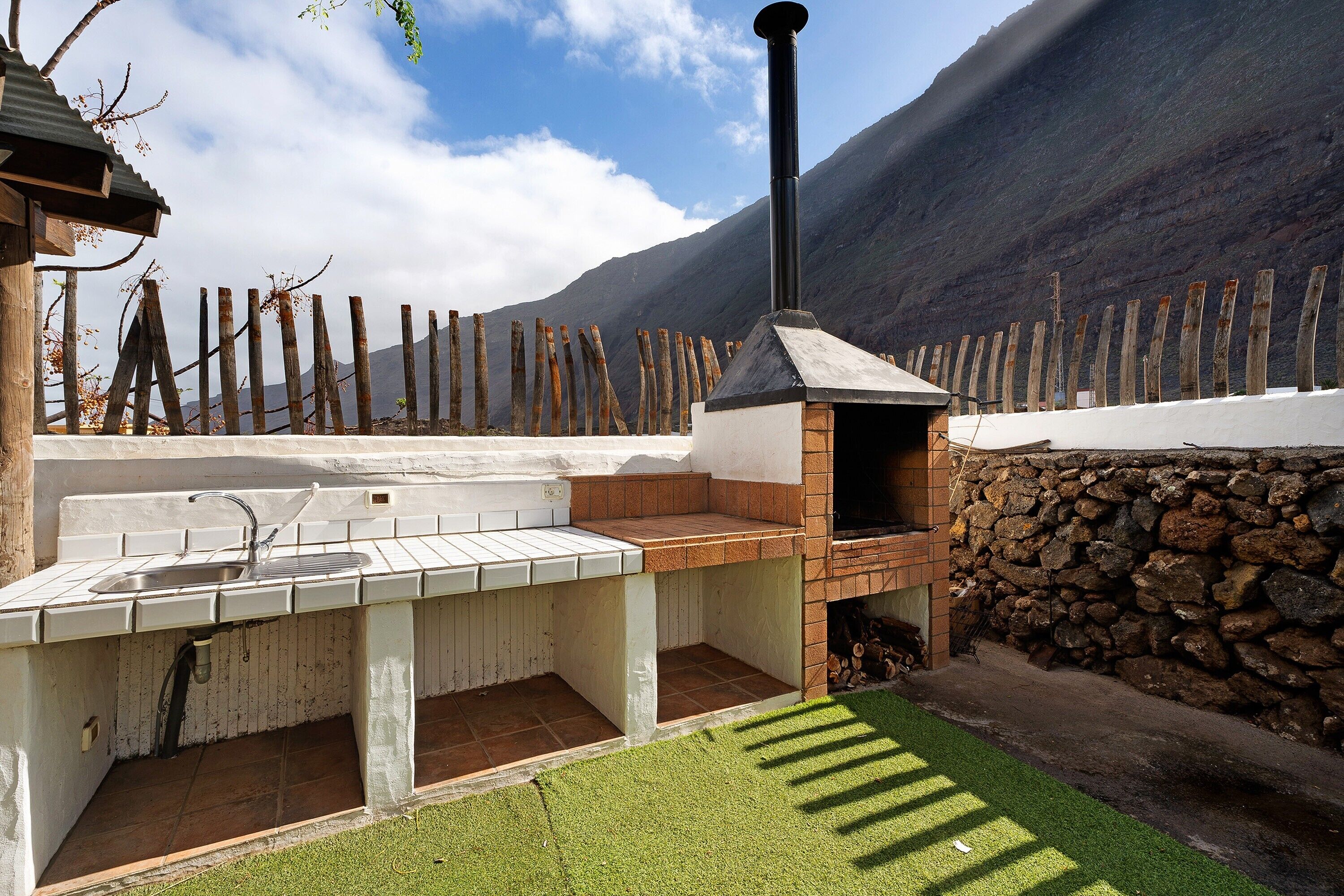 Una cocina al aire libre con pared de piedra, chimenea y vista a la montaña.
