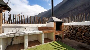 Una cocina al aire libre con pared de piedra, chimenea y vista a la montaña.