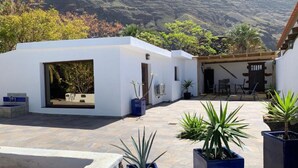 Un patio con un edificio blanco, plantas en macetas y vistas a las colinas.