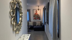 A hallway with a white wall, a decorative mirror, a framed picture, a sofa, and a window with curtains. - Apartment 'Finca Wapa - Apartamento Mayor' with Sea View, Wi-Fi and Air Conditioning (Frontera)