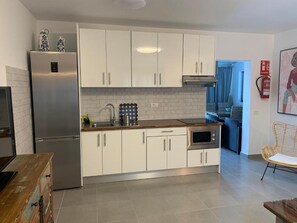 A modern kitchen with white cabinets, a stainless steel refrigerator, a microwave, and a sink.