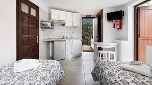 Une chambre d’hôtel compacte comprenant deux lits, une kitchenette, un petit coin repas et une vue sur l’extérieur.