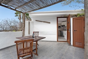 Un patio con una mesa y sillas de madera, una puerta que da a una cocina y una pared blanca.