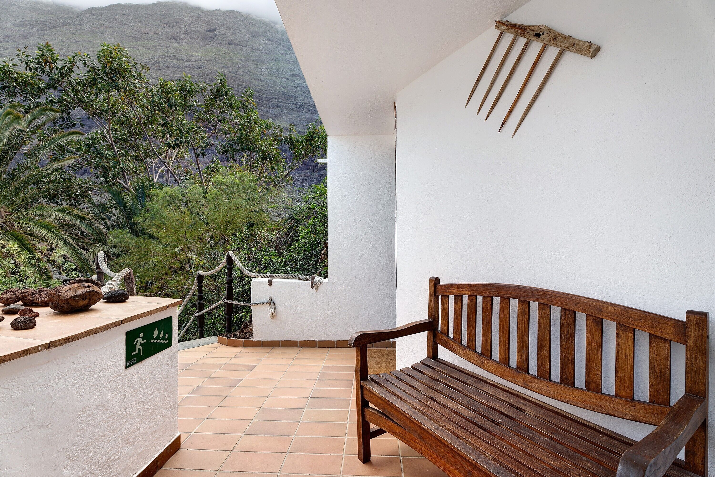A wooden bench, a white wall, and a view of a mountainous landscape.