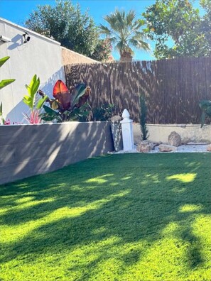 A well-maintained lawn with a concrete wall, a wooden fence, and various plants.