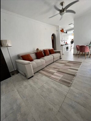 A modern living room with a sofa, a patterned rug, and a ceiling fan.