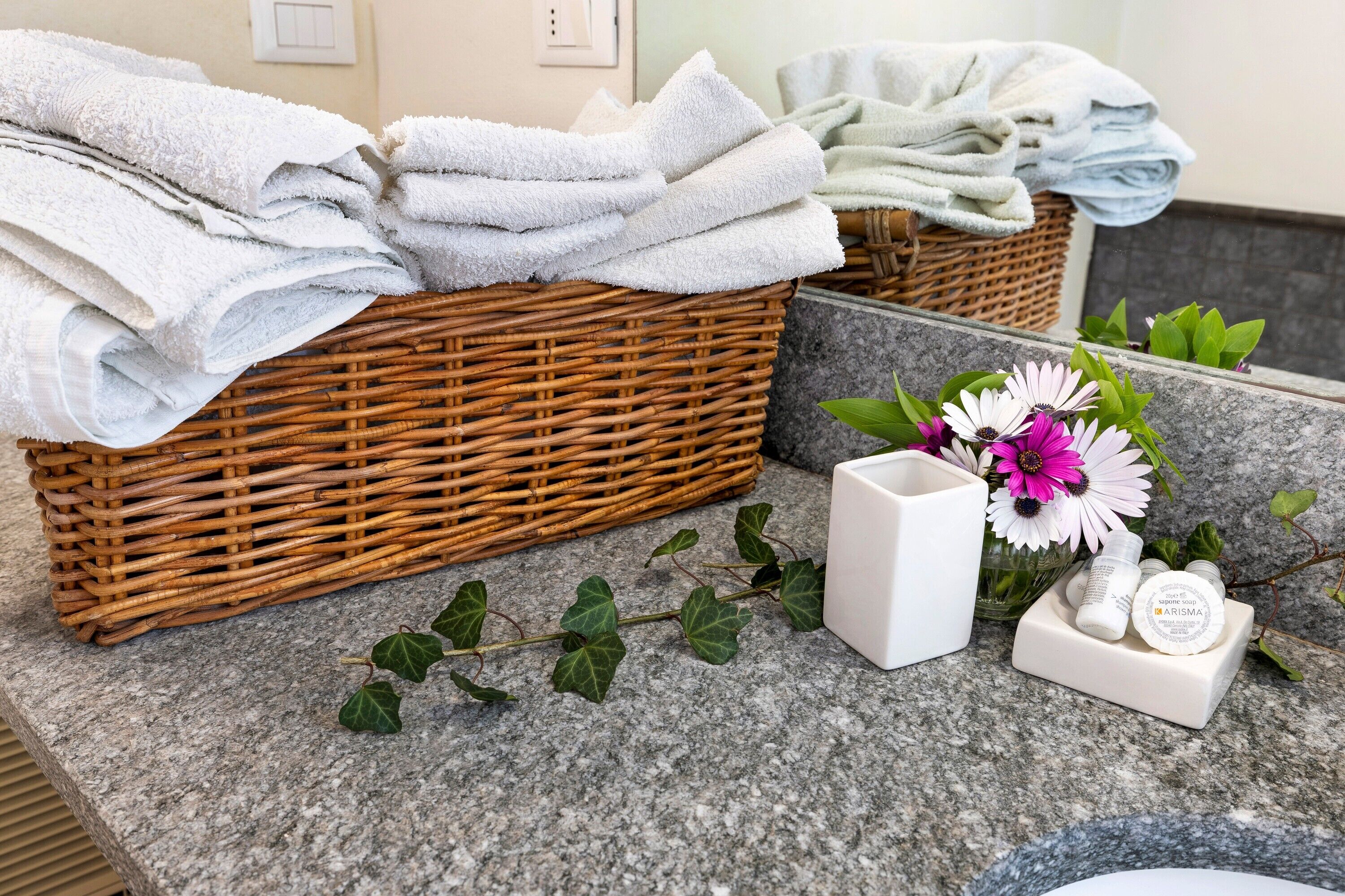 Ein Badezimmer mit einem Korbwäscher voller gefalteter Handtücher, einem weißen Behälter mit einem Produkt und einer Vase mit Blumen.