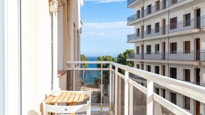 Un balcón con una mesa y sillas de madera, con vistas a un edificio con varios balcones y vista al mar.