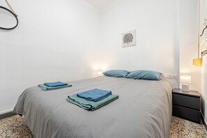 Un lit bien fait, avec des serviettes bleues pliées, une lampe de chevet et une œuvre d’art accrochée au mur.