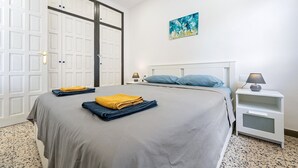 Un dormitorio con una cama, una mesita de noche, una lámpara, un cuadro y una puerta.
