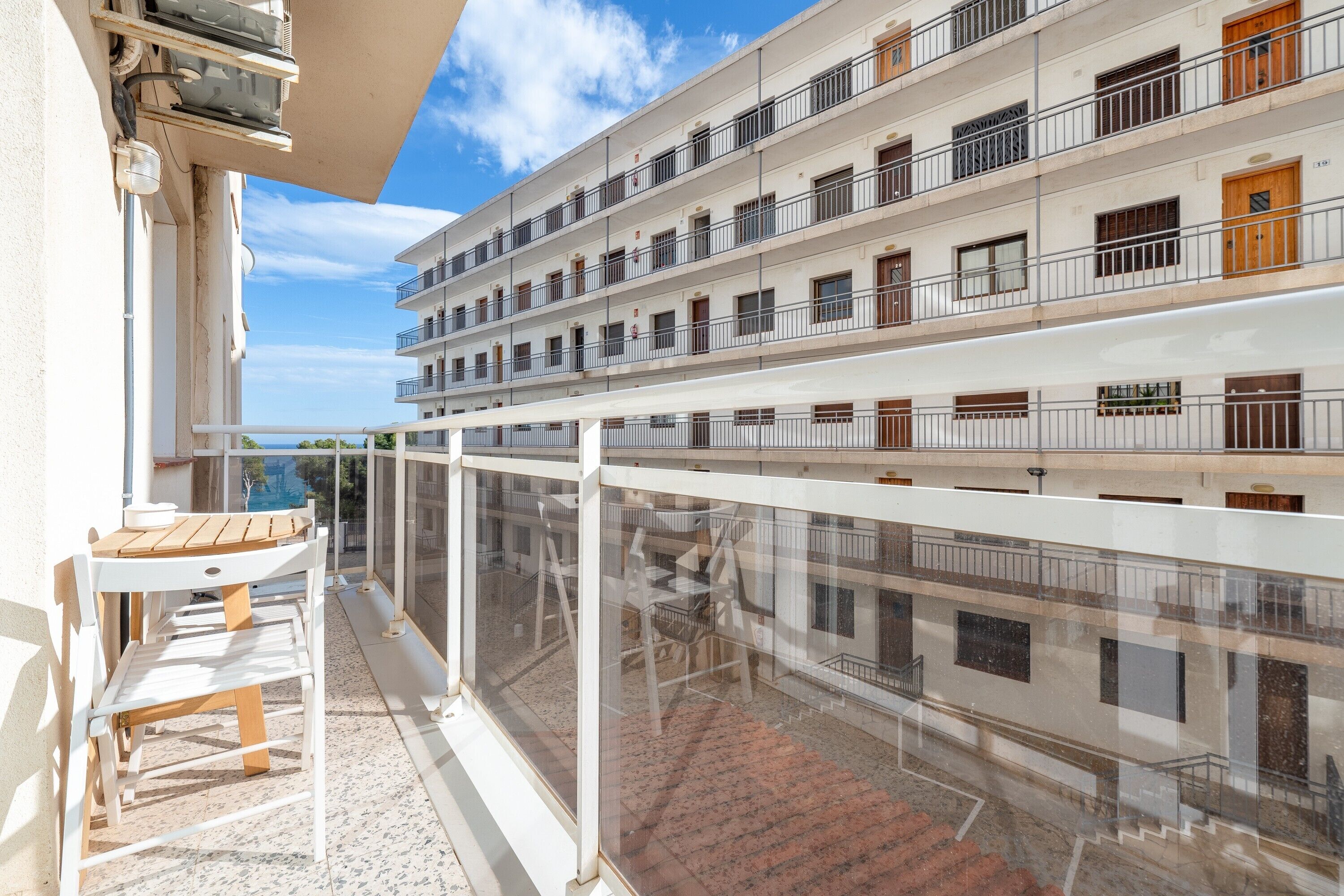 A multi-story hotel with balconies, outdoor seating, and a clear view of the sea.