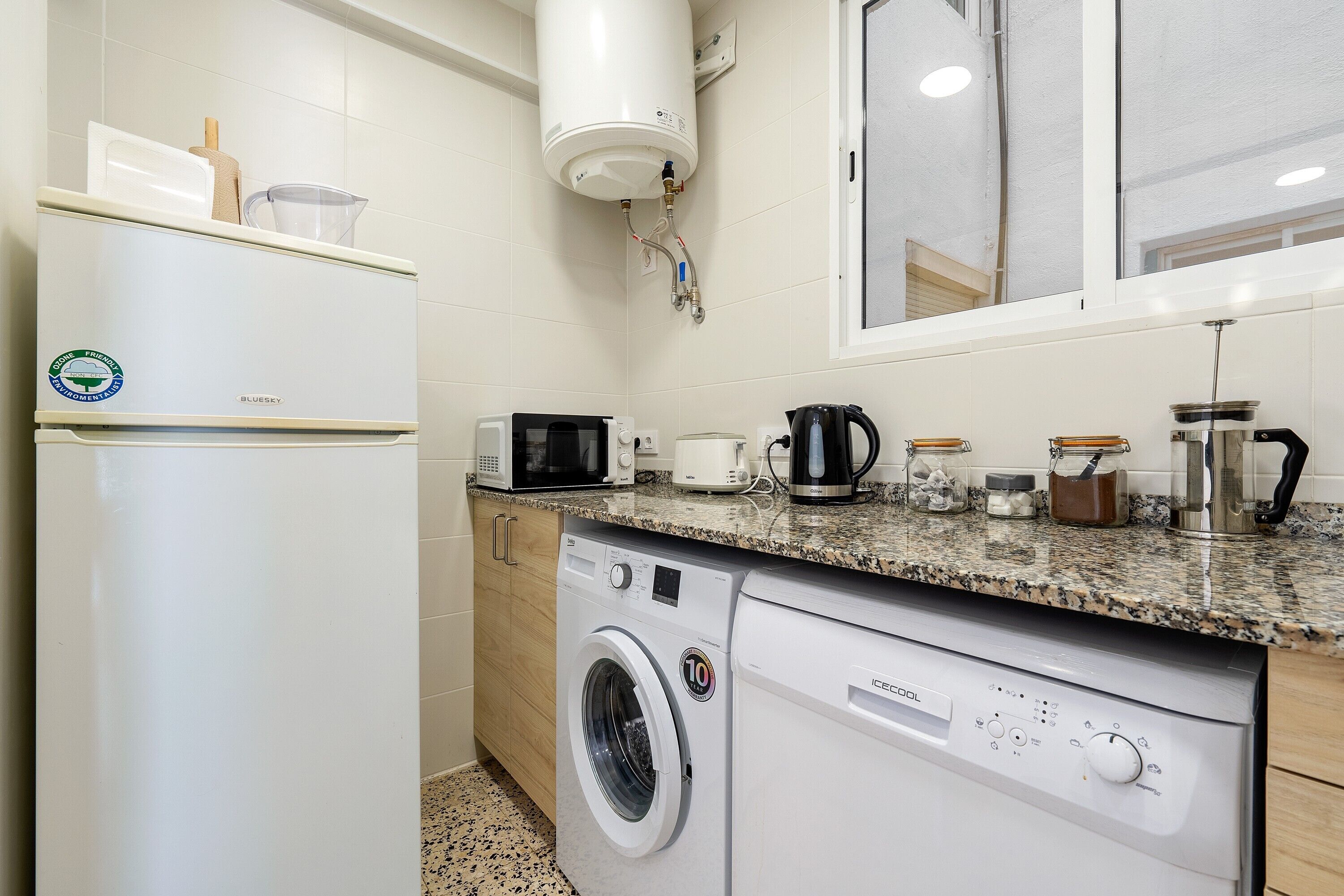 Une cuisine compacte équipée d’un réfrigérateur, d’un four à micro-ondes, d’une machine à café et d’un lave-linge.