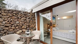 A stone wall, a glass door leading to a bedroom, and a round table with chairs. - Apartment 'Finca Wapa - Studio 2' with Sea View, Wi-Fi and Air Conditioning (Frontera)