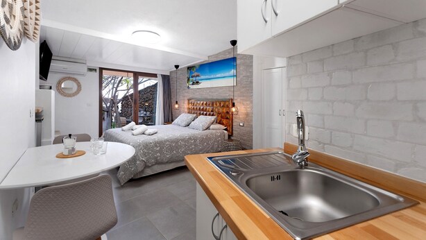 A compact hotel room with a kitchenette, a bed with a view, a dining area, and a bathroom with a shower. - Apartment 'Finca Wapa - Studio 2' with Sea View, Wi-Fi and Air Conditioning (Frontera)