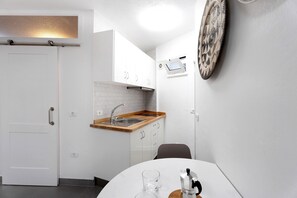 Une cuisine compacte avec des meubles blancs, un plan de travail en bois, un évier et un four fixé au mur.