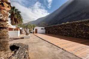 Une cour avec un mur de pierre, un bâtiment blanc et une montagne en arrière-plan.