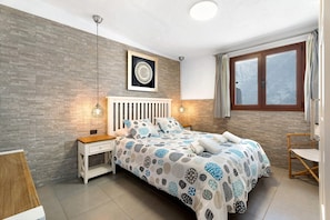 A bedroom with a bed, bedside tables, a hanging light, a window, and a wall-mounted picture.