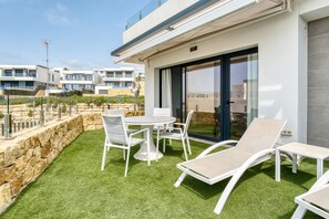 A modern outdoor patio with a round table and chairs, lounge chairs, and a stone retaining wall. - Apartment 'Izabell' with Mountain View, Shared Pool and Wi-Fi (Finestrat)