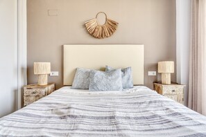 A bed with a striped blanket, two bedside tables with lamps, and a wall-mounted decorative piece. - Apartment 'Izabell' with Mountain View, Shared Pool and Wi-Fi (Finestrat)