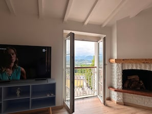 A living room with a TV, a fireplace, and a balcony with a view.