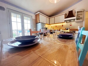 A kitchen with wooden cabinets, a dining table with clear plastic covers, and a view of the outside through a sliding door.