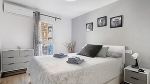 A modern bedroom with a bed, a bedside table with a lamp, a dresser, and a window with curtains. - Apartment 'Aquario' with Sea View, Wi-Fi and Air Conditioning (Benalmádena)