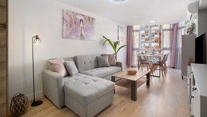 A modern living room with a grey sectional sofa, a wooden coffee table, and a dining area with a glass table and chairs. - Apartment 'Aquario' with Sea View, Wi-Fi and Air Conditioning (Benalmádena)
