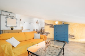 Un salon avec un canapé, une table basse en verre, une commode bleue et un mur en briques.
