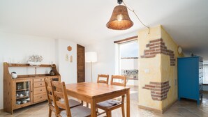 Un comedor con una mesa y sillas de madera, una lámpara colgante, una zona de cocina con armarios y un mueble azul.