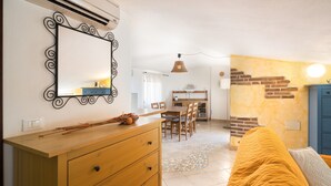 Una habitación con un aparador de madera, un espejo, una zona de comedor con sillas y una mesa, y una cama con una colcha amarilla.