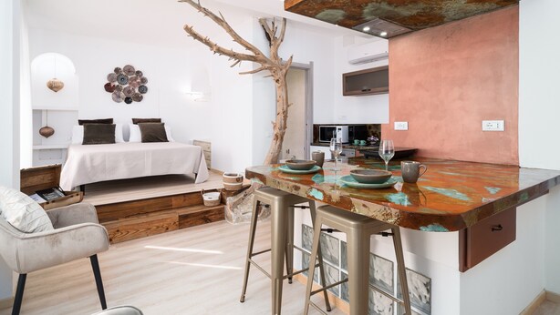 Une cuisine moderne avec un coin bar au style rustique, une table à manger et un lit doté d’une tête de lit blanche.