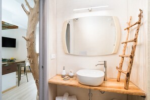 Un baño con un espejo redondo, un lavabo blanco, una escalera de madera y una decoración con trozo de tronco de árbol.