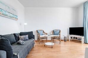 Olohuoneessa on sohva, kaksi rottinkituolia, pieni pyöreä pöytä, jalustalla oleva televisio ja lattiavalaisin.
