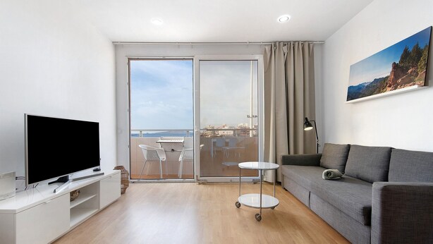 Un salon moderne doté d’un téléviseur à écran plat, d’un canapé gris et d’un balcon offrant une vue agréable.