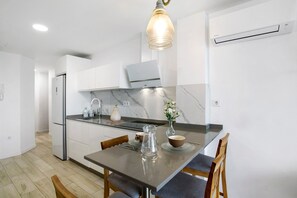 Une cuisine moderne avec des meubles blancs, un pare-feu en marbre et un coin repas comprenant une table et des chaises.