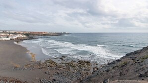 A coastal landscape with a beach, rocky shoreline, and a distant cityscape.