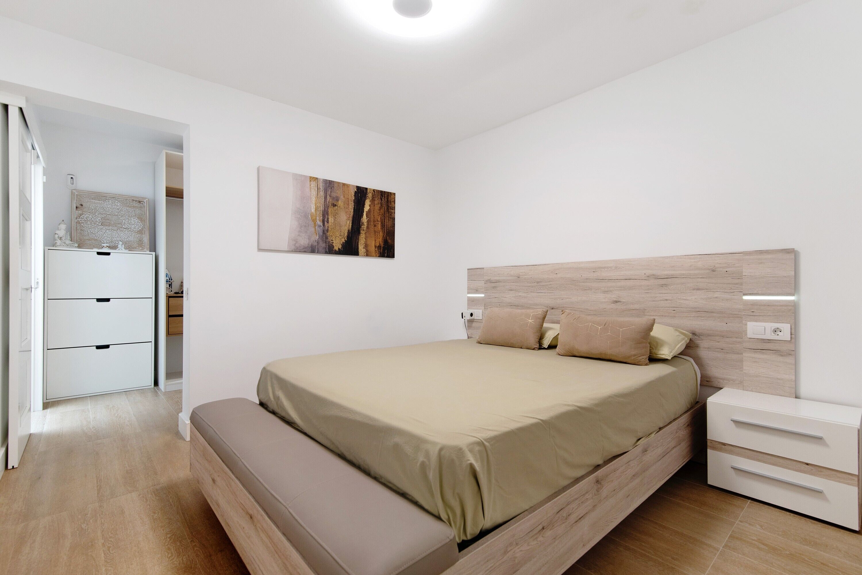 A bedroom with a bed, bedside table, bench, and a painting on the wall.