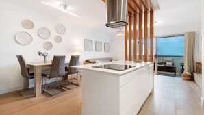 A modern kitchen with a central island, wooden ceiling beams, and a dining area with chairs and a table.