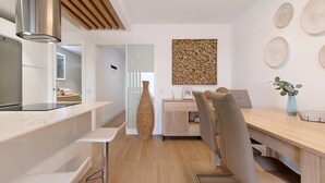A modern kitchen with a stainless steel range hood, a wooden ceiling, and a dining area with a wooden table and chairs.