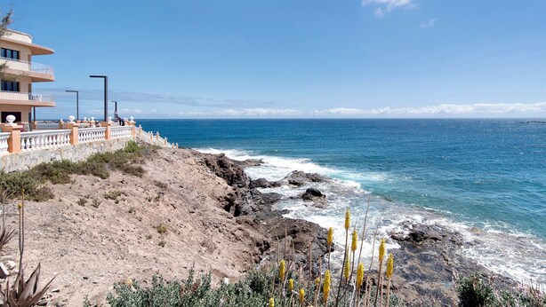 A coastal hotel with a rocky shoreline, a balcony with a railing, and a view of the sea.