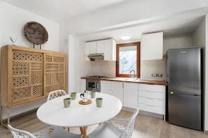 Una cocina funcional con una mesa blanca, sillas, un refrigerador y un microondas.