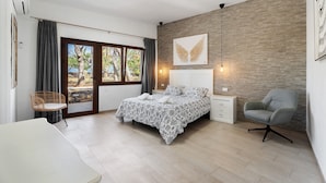 A bedroom with a bed, a chair, a desk, and a view through a glass door.