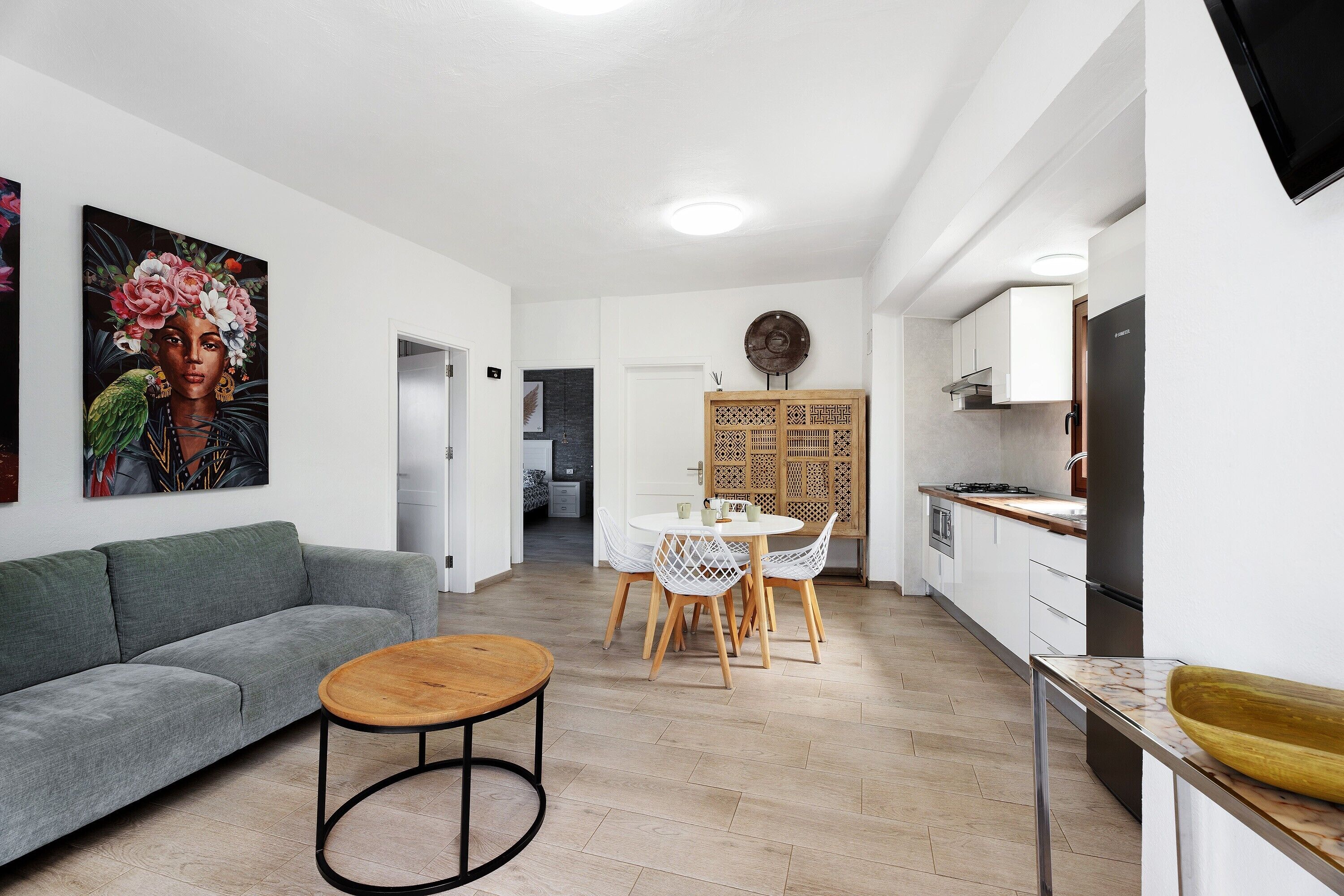 A modern living room with a grey sofa, a wooden coffee table, and a dining area with a white table and chairs.